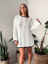 Vestido corto tejido al crochet color blanco, con mangas largas y escote redondo con borde negro.