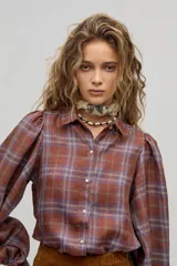 Camisa larga de lino a cuadros color avellana, con cuello camisero clásico, mangas largas abullonadas con puños elásticos, botones de nácar frontales y ruedo curvo, un poco más largo atrás. Incluye cinturón de cuero marrón.