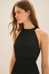 Vestido largo negro con escote halter con volados en cuello y fuelle con cinta interna para ajustar escote. Tiene volados y costuras elásticas en cintura y ruedo con volado.