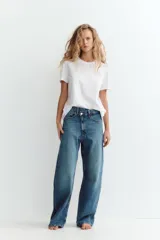 Jeans de tiro medio color azul denim, corte baggy, con trabillas y cinco bolsillos. Cierre frontal asimétrico con cremallera y botones metálicos.