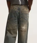 Pantalón super baggy de jeans con lavado dirty en tonos tierra, cintura con trabilla, cierre tradicional, bolsillos y bordado en el bolsillo trasero.