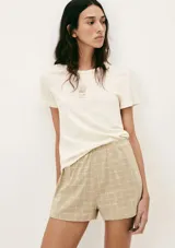 Pijama de dos piezas compuesto por una remera de manga corta color crema con un pequeño bordado de concha marina y un short de tiro alto con elástico y estampado de cuadrícula en tonos beige y blanco.