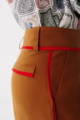 Pantalón de vestir color marrón con corte recto y cintura alta. Presenta una fina cinta roja a modo de cinturón.