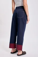 Pantalón de jean azul oscuro, de corte recto y holgado, con el bajo doblado mostrando un forro color bordó.