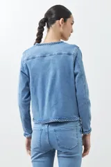 Chaqueta de jean celeste con cuello redondo, cierre con botones metálicos y detalle trenzado en cuello, bolsillos y ruedo.
