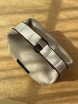 Neceser color beige de forma rectangular, con cierre superior y asa de mano.