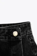 Falda pantalón de tiro alto confeccionada en denim negro. Presenta bolsillos delanteros y traseros de parche. El cierre frontal es cruzado con cremallera oculta y botón metálico.