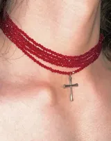 Gargantilla de cuentas rojas con dije de cruz plateada.