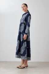 Maxi vestido azul marino con estampado de arabescos en blanco, corte camisero, cuello clásico, mangas 3/4 y falda escalonada.