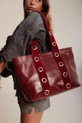 Cartera grande de cuero color bordó, con asas de gamuza y ojales metálicos dorados.