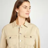 Mono largo color beige de jean con cuello camisero, cierre frontal con botones a presión, mangas largas con puños abotonados, bolsillos en el pecho y corte recto.