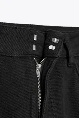 Pantalón de jean negro de corte palazzo, tiro medio y cintura con trabillas. Tiene bolsillos delanteros y traseros, raya planchada en el frente y cierre frontal con cremallera, botón y ganchos metálicos.