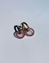 Par de aros colgantes con argollas doradas y dijes circulares de resina transparente con incrustaciones de strass de colores. El dije mide aproximadamente 1.5cm de diámetro.