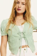 Top corto verde agua en punto arrugado con escote en V y doble cordón de ajuste abajo del busto que se enlaza adelante. Mangas cortas con elástico revestido y ribete sobrehilado.