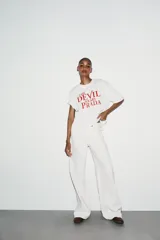 Camiseta blanca de algodón con cuello redondo, mangas cortas y hombros caídos. Estampado frontal con el título de la película "El Diablo Viste de Prada" en letras rojas.