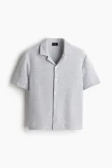 Camisa de manga corta color gris claro, de punto con textura de mezcla de algodón. Modelo con cuello abierto, tapeta lisa y bajo recto. Corte estándar para una silueta clásica y cómoda.