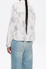 Camisa blanca con estampado de cactus en color gris, corte boxy, cuello camisero, manga larga con puño y cierre frontal con abotonadura.