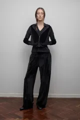 Campera de terciopelo negro brilloso con capucha, cierre frontal, bolsillos laterales, puños y cintura ajustados. Silueta relajada.