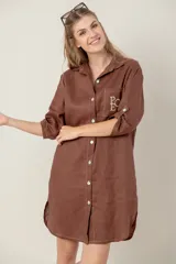 Vestido camisero marrón de lino con botones, mangas 3/4 y bolsillo en el pecho con bordado de letras.