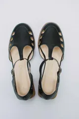 Sandalias bajas negras de cuero con pulsera al tobillo y talón cubierto. Presentan aberturas circulares en la capellada y taco de madera.