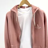 Campera con capucha color rosa viejo, con cierre frontal y bolsillos laterales. Logo de la marca bordado en el pecho.