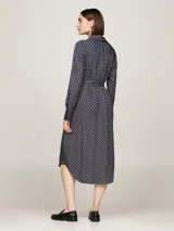 Vestido camisero midi azul marino con estampado geométrico en blanco, cuello camisero, manga larga con puños abotonados, cierre frontal con botones, cinturón de lazo y bajo asimétrico.