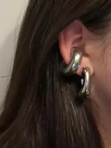 Aros tipo cuff plateados, gruesos y con diseño moderno.