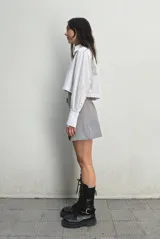 Falda sastrera gris con pinzas que forman tablas en el delantero y cinturón desmontable asimétrico.