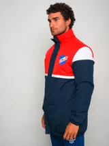 Campera parka de hombre con cuello alto, cierre frontal con cremallera y broches a presión, y escudo del Club Nacional de Football en el pecho. Diseño a bloques de color azul marino, blanco y rojo.