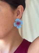 Aros con forma de flor pintada a mano en color celeste con detalles en fucsia y mostacillas en el centro.