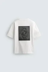 Camiseta blanca de corte holgado, cuello redondo y manga corta. Presenta un parche bordado en la espalda con diseño a contraste.