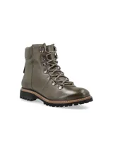 Borcego alpino color verde oliva de cuero napa con detalles metálicos, base de goma estilo trucker con pespuntes naturales en contraste y cordones de algodón al tono. Diseñado en Uruguay y fabricado en Brasil.