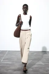 Pantalón color beige de tiro alto, corte ancho y largo midi, con pinzas delanteras, bolsillos laterales y traseros. Cierre frontal con cremallera y botón.
