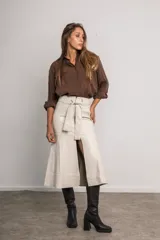 Falda midi color marfil de cuerina, con cierre metálico frontal, cinturón con lazo y abertura delantera.