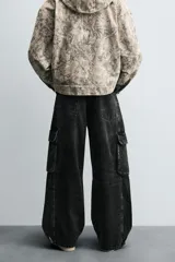Pantalón relaxed fit de denim negro con efecto lavado, bolsillos frontales, traseros de plastrón y multifunción en perneras. Bajo ajustable con trabilla y cierre frontal con cremallera y botón.