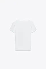 Camiseta blanca de algodón con cuello redondo y mangas cortas. Presenta un bolsillo de tul con una flor bordada y abalorios en el delantero.