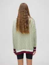 Sweater tejido de algodón color rosa claro, con cuello polo con cierre de cremallera metálica y mangas largas con puños a rayas de colores.