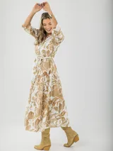 Vestido largo camisero con estampado floral en tonos beige y blanco, con cuello camisero, mangas 3/4 y falda escalonada. Incluye cinturón de soga con hebilla de madera.