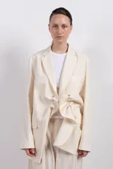 Blazer color crema de corte amplio con diseño asimétrico y detalle de nudo frontal.