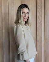 Blusa color beige con cuello con volados, mangas largas abullonadas con puños elásticos y cierre con botones en la parte delantera.