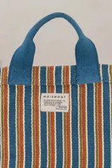 Bolso tote pequeño de algodón a rayas verticales en tonos azul, naranja, verde y blanco. Tiene doble asa corta azul y correa larga ajustable del mismo color.