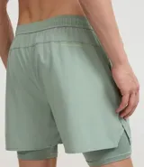 Short deportivo para hombre, color gris claro, con short de compresión negro incorporado. Presenta un pequeño logo bordado en la pierna derecha.