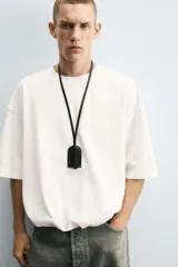 Camiseta blanca de algodón, corte holgado, cuello redondo, manga corta y bajo con elástico interior.