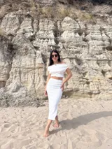 Conjunto de dos piezas color blanco, compuesto por un top corto con escote Bardot (hombros descubiertos) y una falda midi ajustada con textura fruncida (bambula elastizada).