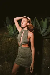 Minivestido dorado de tejido de punto con lurex, cuello halter con abertura central, cut-outs laterales y espalda descubierta.