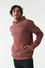 Canguro color ladrillo de felpa con capucha, bolsillo tipo canguro, bolsillo con botón en la manga y lettering estampado en la espalda.