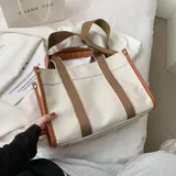 Bolso tipo tote color beige con laterales negros, doble asa corta de mano con detalles en cuero sintético negro y correa larga de hombro negra regulable y extraíble.