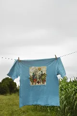 Remera celeste de manga corta con estampa de un paisaje con montañas, árboles y el sol.