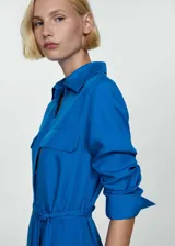 Vestido camisero midi color azul eléctrico, con cuello camisero, manga larga con puños abotonados, dos bolsillos de parche en el pecho, lazo ajustable en la cintura, cierre frontal con botones y aberturas laterales en el bajo.
