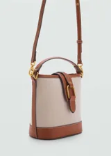 Bolso tipo bucket color crudo con base marrón, confeccionado en tejido mezcla de algodón con efecto rafia. Tiene asa corta superior, asa larga desmontable y cierre de solapa con botón magnético.